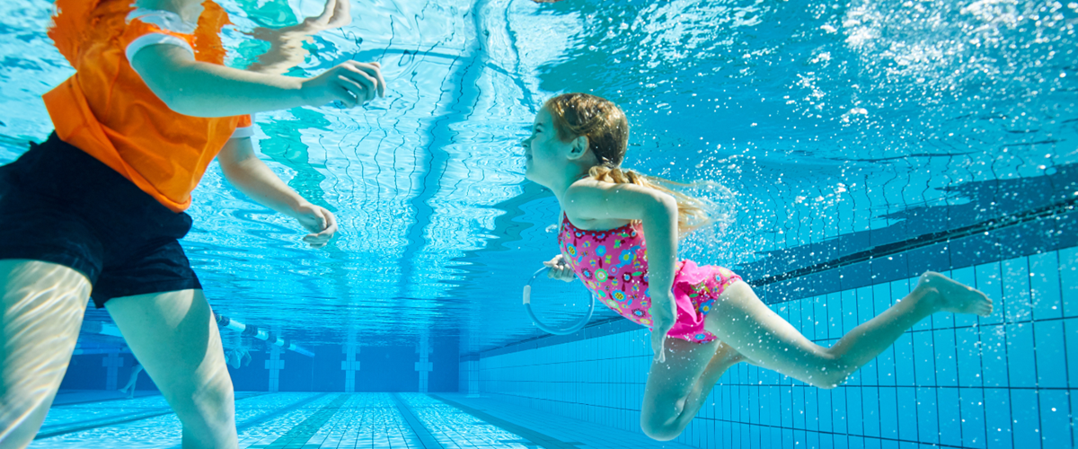 Child swimming underwater with swim teacher or instructor